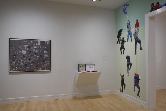 Installation of exhibition by Tyler Starr with people on wall and flags.